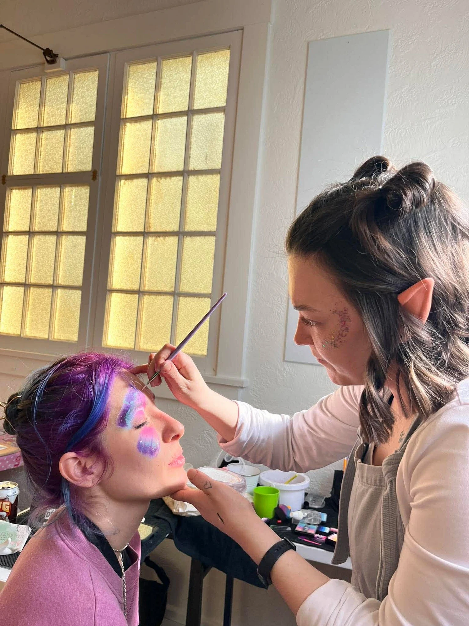 Tay carefully painting a fairy butterfly design on a smiling client