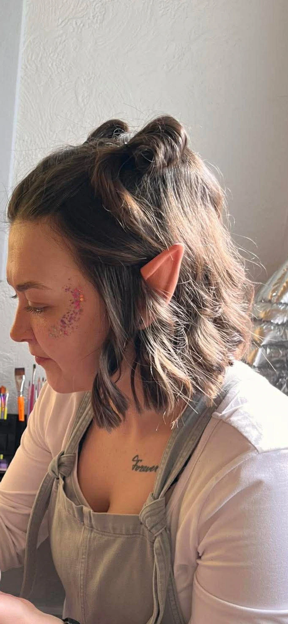 Tay wearing elf ears and grey overalls concentrating while face painting
