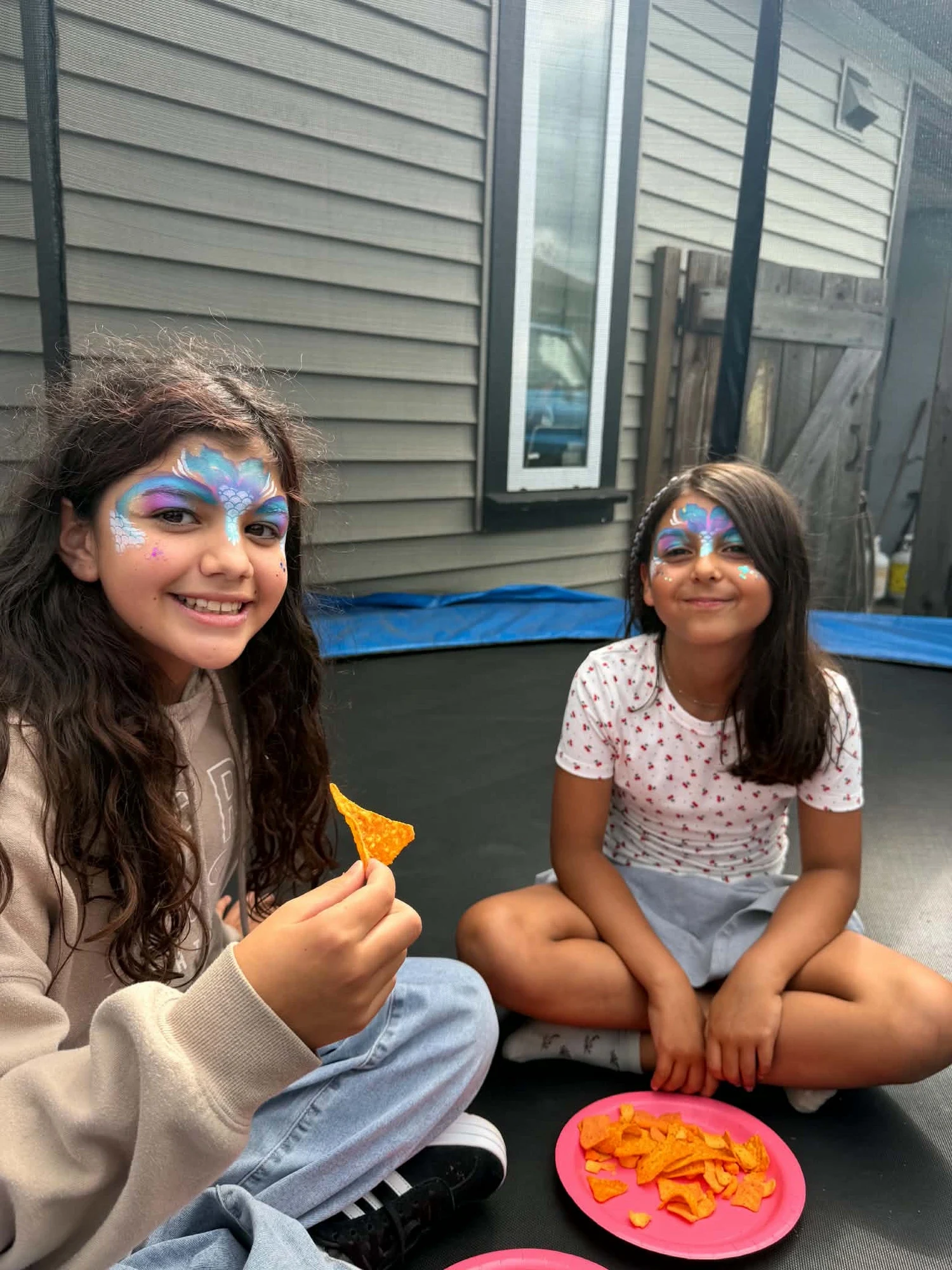 Two girls with blue and purple mermaid mask face painting on a trampoline