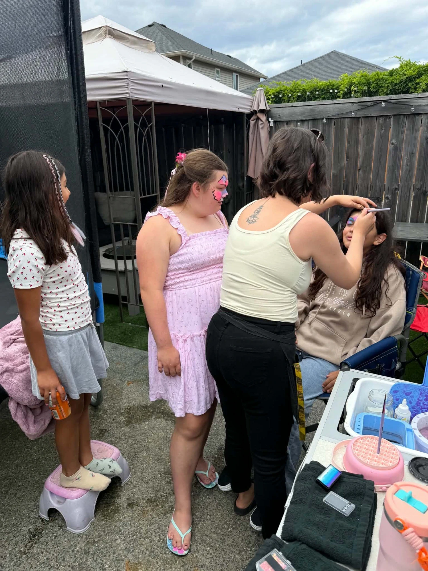 Tay painting a butterfly design on a child at an outdoor backyard party