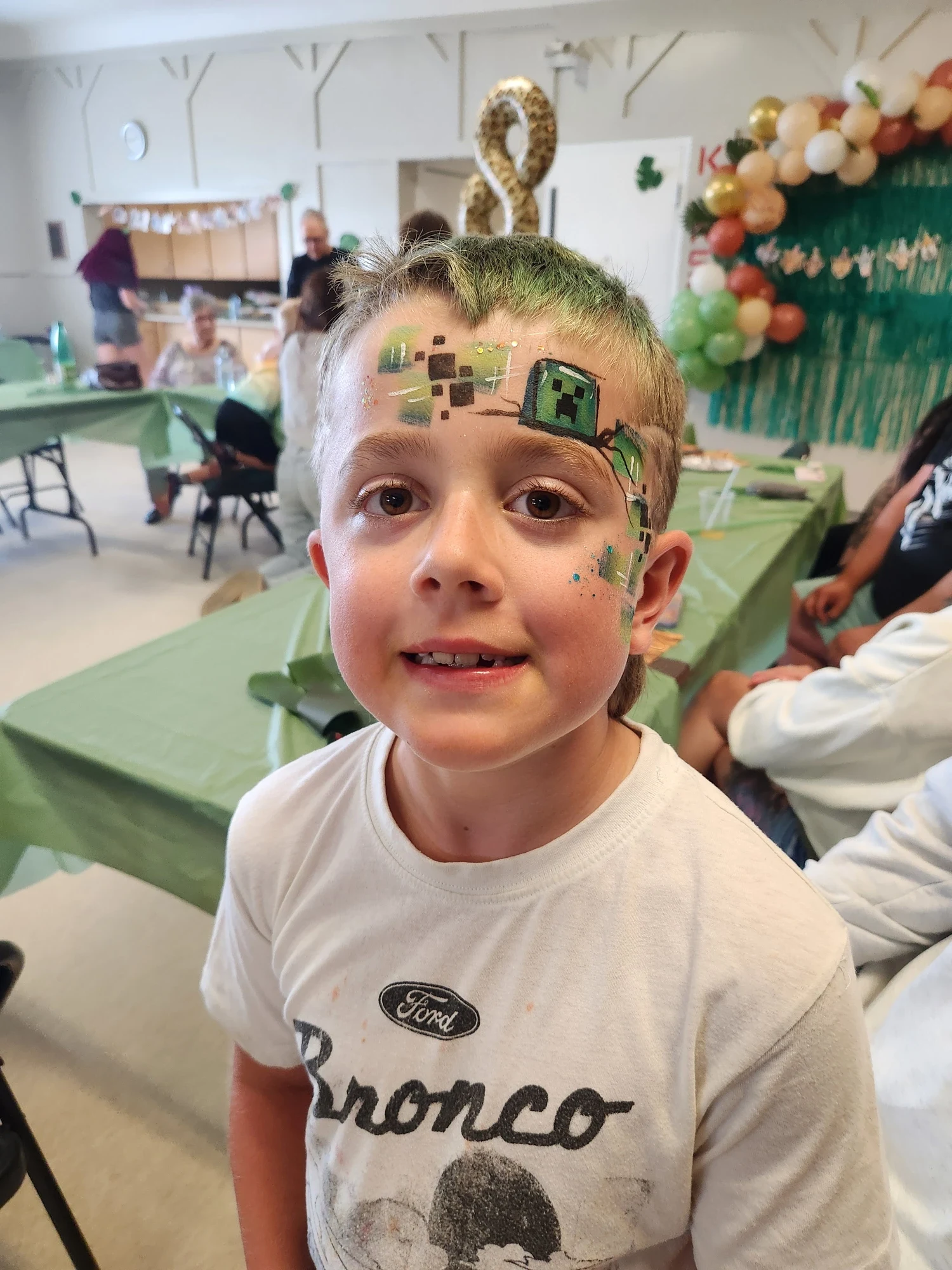 Boy with a green Minecraft creeper face painting at a birthday party